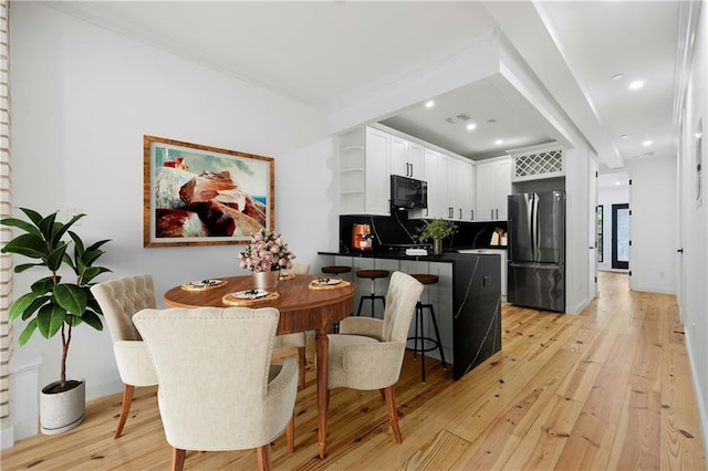 kitchen with stainless steel refrigerator, light wood-type flooring, crown molding, white cabinets, and backsplash