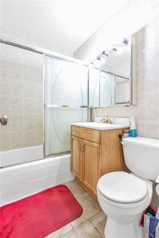 full bathroom with vanity, bath / shower combo with glass door, tile patterned floors, toilet, and tile walls