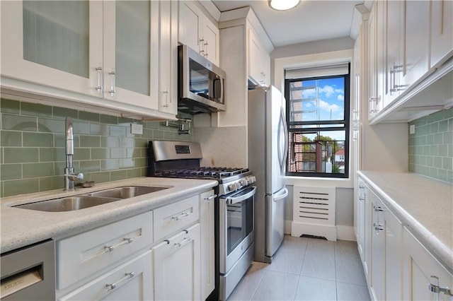 kitchen with a sink, white cabinetry, appliances with stainless steel finishes, light tile patterned floors, and glass insert cabinets