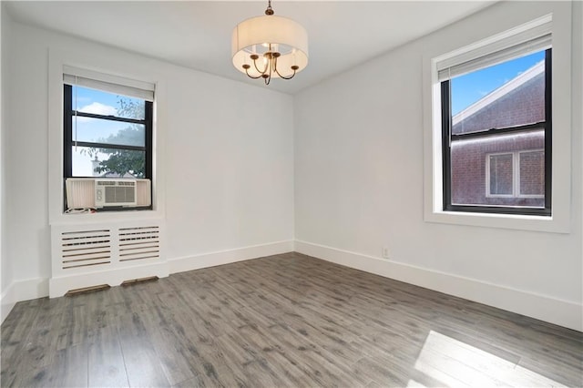 spare room featuring cooling unit, baseboards, an inviting chandelier, and wood finished floors