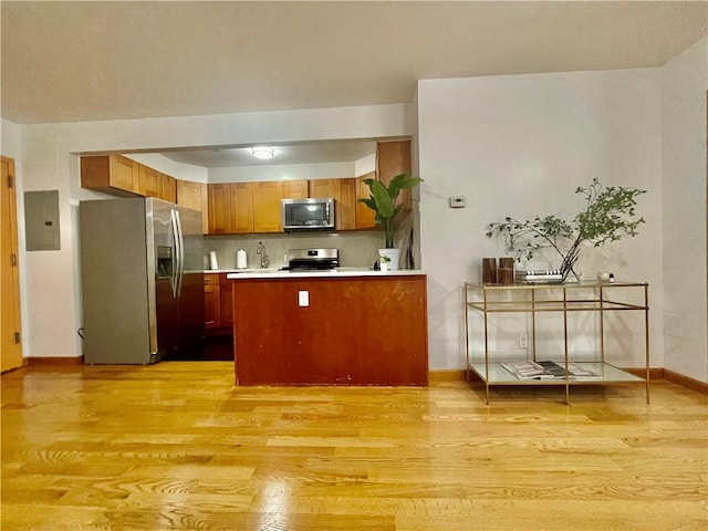 kitchen with kitchen peninsula, stainless steel appliances, electric panel, and light hardwood / wood-style flooring