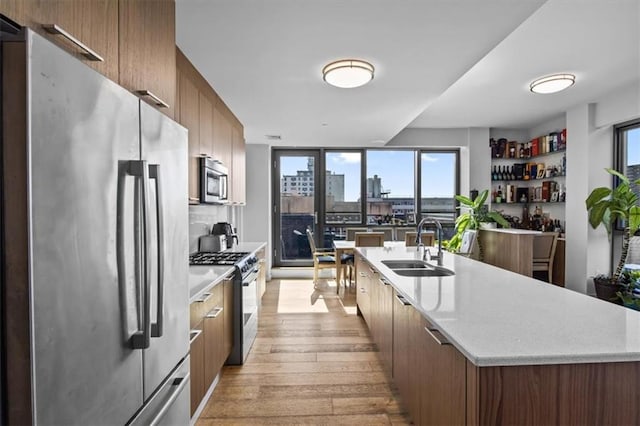 kitchen featuring a view of city, light wood-style flooring, appliances with stainless steel finishes, a sink, and a large island with sink