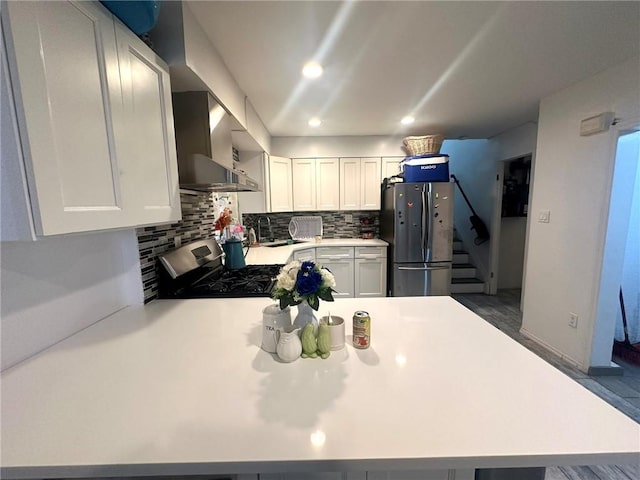 kitchen with stainless steel appliances, tasteful backsplash, white cabinets, sink, and wall chimney range hood