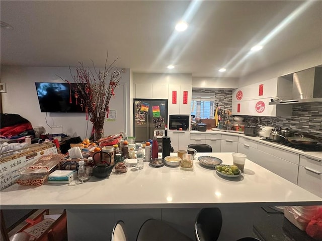 kitchen with white cabinets, black refrigerator, gas cooktop, wall chimney range hood, and backsplash