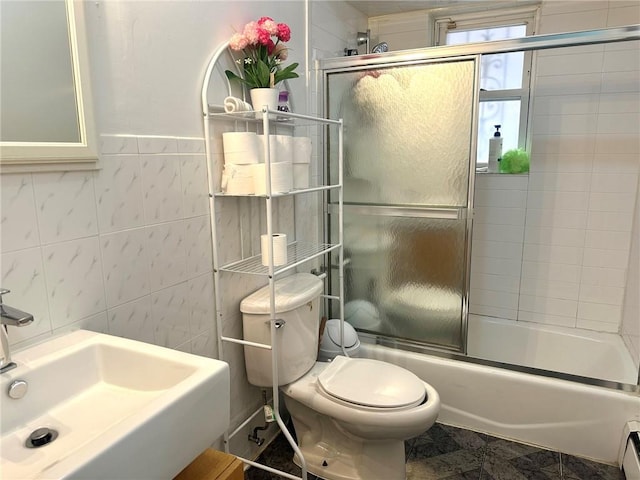 full bathroom with a baseboard heating unit, tile walls, sink, toilet, and shower / bath combination with glass door