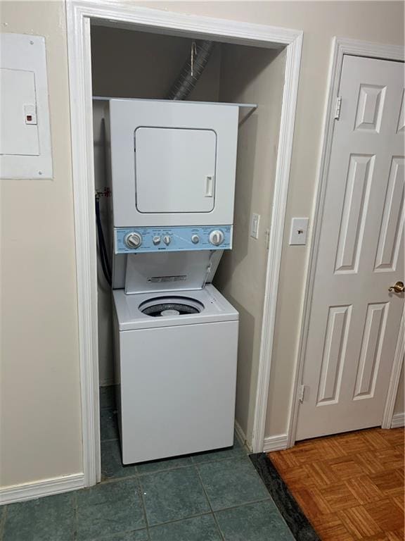 laundry room with electric panel, baseboards, and stacked washer / drying machine