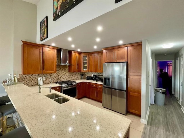 kitchen with sink, a breakfast bar area, wall chimney exhaust hood, light stone countertops, and stainless steel appliances