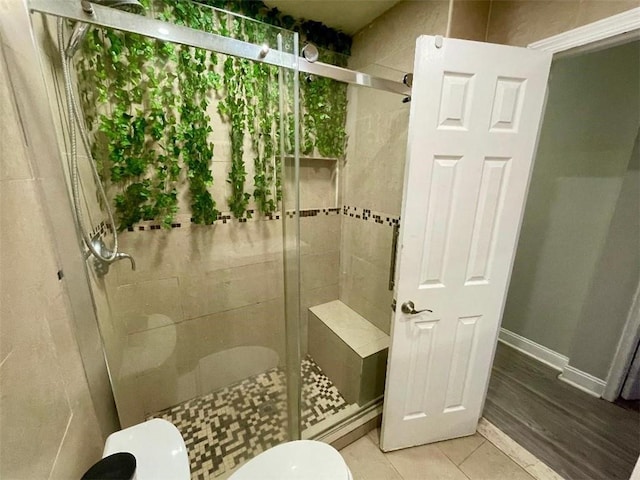 bathroom featuring tile patterned flooring, toilet, and a shower with shower door