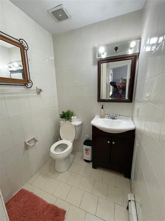 bathroom with tile patterned flooring, baseboard heating, tile walls, and toilet