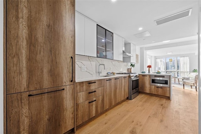 kitchen featuring sink, light hardwood / wood-style flooring, high end stainless steel range oven, white cabinetry, and decorative backsplash