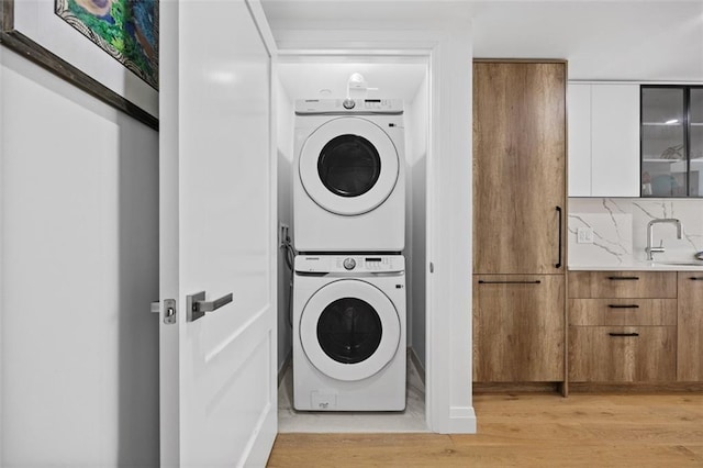 laundry area featuring stacked washer and dryer, sink, and light hardwood / wood-style floors