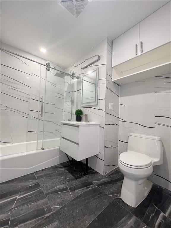 full bathroom with bath / shower combo with glass door, vanity, tile walls, and toilet