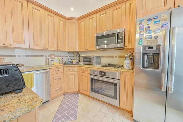 kitchen with appliances with stainless steel finishes, light tile patterned floors, light stone counters, and light brown cabinets