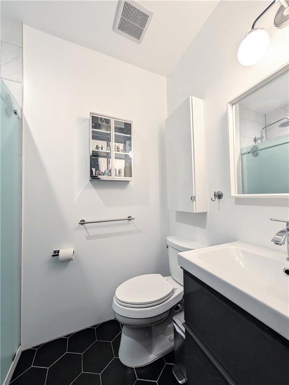 bathroom with tile patterned flooring, vanity, a shower with shower door, and toilet