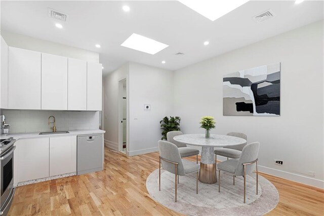 kitchen with sink, white cabinetry, a skylight, light hardwood / wood-style flooring, and stainless steel appliances