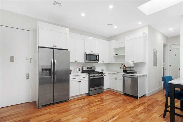 kitchen featuring appliances with stainless steel finishes, a skylight, white cabinetry, sink, and light hardwood / wood-style flooring