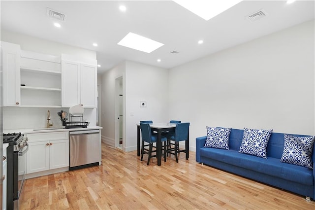 kitchen with sink, appliances with stainless steel finishes, white cabinetry, a skylight, and light hardwood / wood-style floors