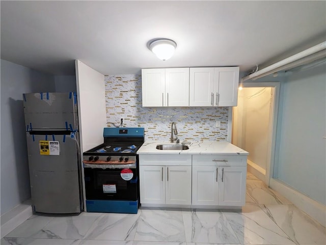 kitchen with sink, stainless steel refrigerator, stove, white cabinetry, and light stone counters