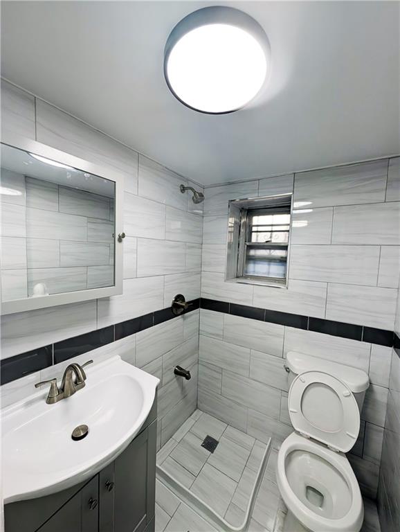 bathroom featuring vanity, toilet, tile walls, and a tile shower