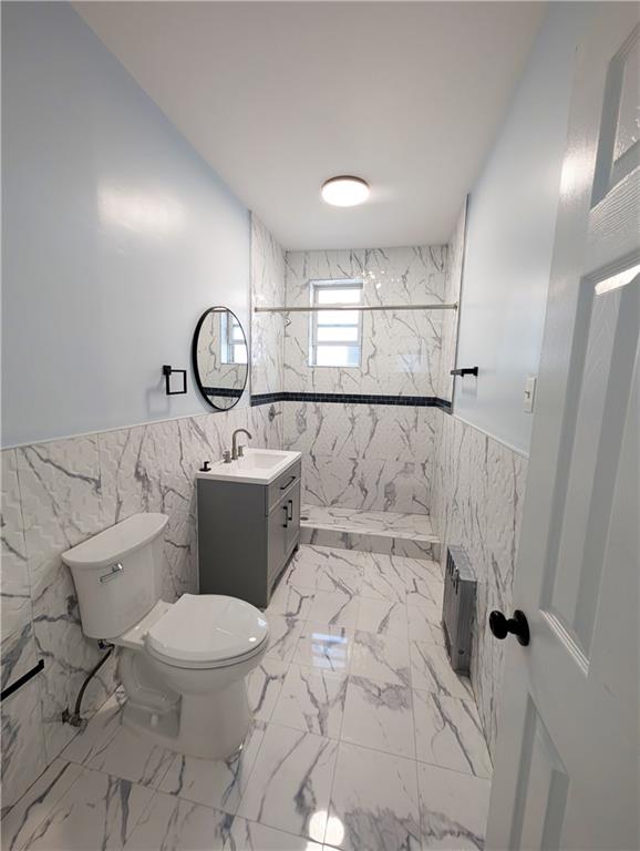 bathroom with tile walls, vanity, toilet, and tiled shower