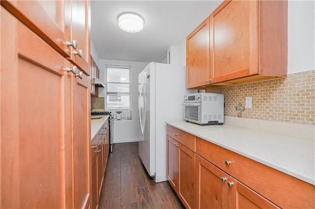 kitchen with tasteful backsplash, dark hardwood / wood-style flooring, stainless steel gas range, and white fridge