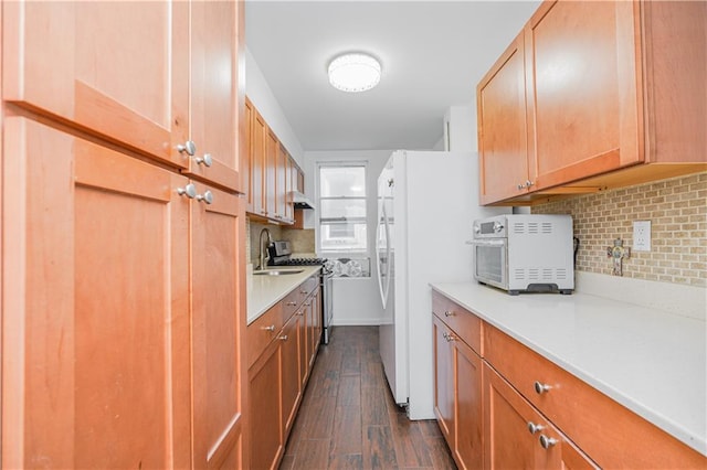 kitchen featuring sink, dark hardwood / wood-style floors, stainless steel range with gas stovetop, white fridge, and decorative backsplash