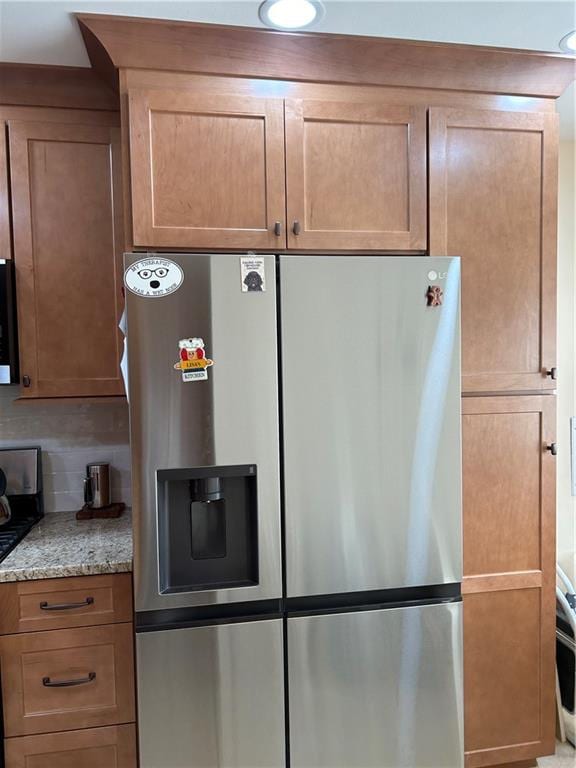 kitchen featuring stainless steel fridge, light stone countertops, and decorative backsplash