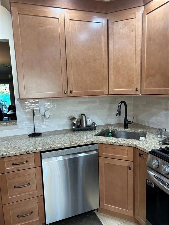 kitchen with sink, appliances with stainless steel finishes, light stone counters, and tasteful backsplash