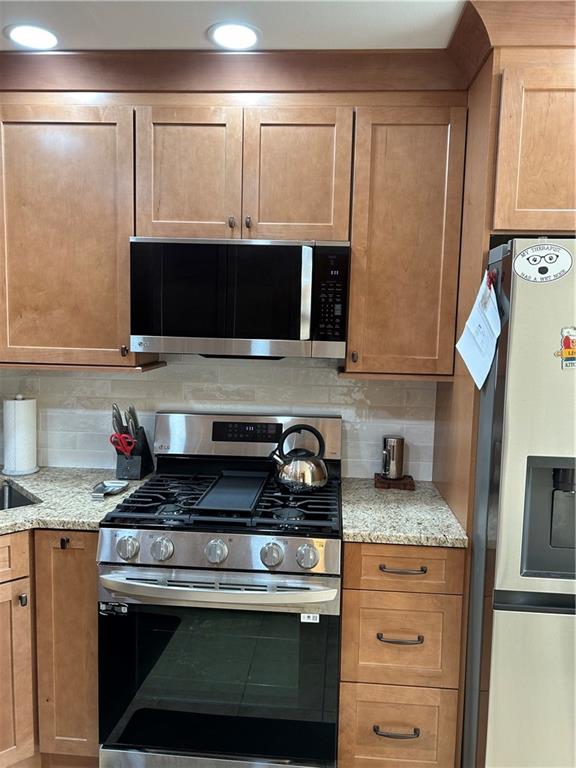 119 Stonegate Dr Unit 119, Staten Island, NY 10304 - kitchen with light stone counters, brown cabinetry, tasteful backsplash, and stainless steel appliances