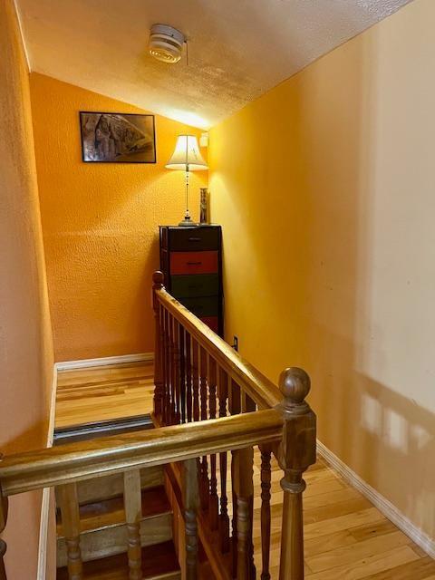 staircase featuring hardwood / wood-style flooring, a textured ceiling, and lofted ceiling