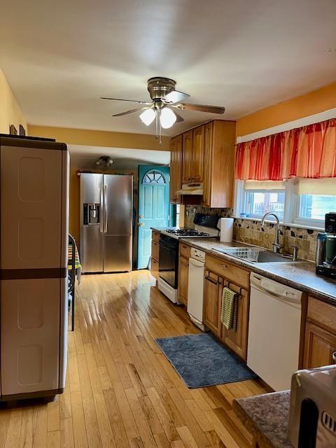 kitchen with white dishwasher, stainless steel refrigerator with ice dispenser, sink, light wood-type flooring, and backsplash