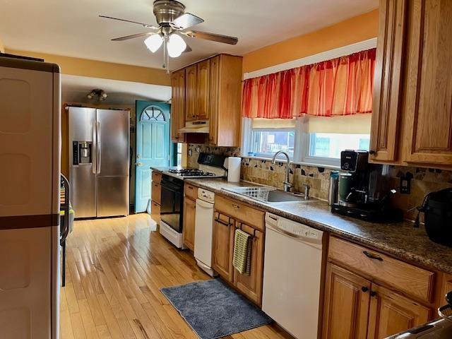 kitchen with stainless steel refrigerator with ice dispenser, dishwasher, a sink, under cabinet range hood, and gas range oven