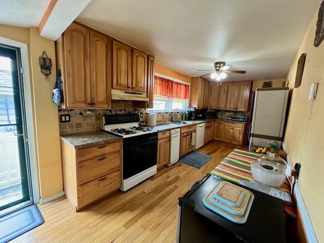 kitchen featuring gas range, light hardwood / wood-style floors, decorative backsplash, and white dishwasher