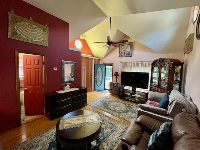 living room featuring a wall mounted AC, wood finished floors, ceiling fan, and high vaulted ceiling