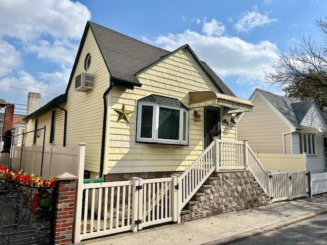 bungalow-style home with a wall mounted AC, fence, and a gate