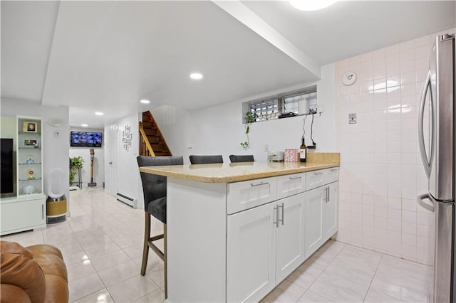 kitchen featuring a kitchen bar, stainless steel fridge, white cabinets, and light tile patterned flooring