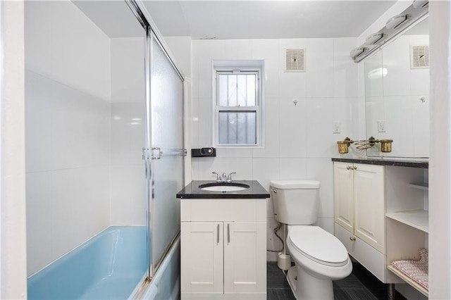 full bathroom featuring shower / bath combination with glass door, vanity, tile walls, and toilet