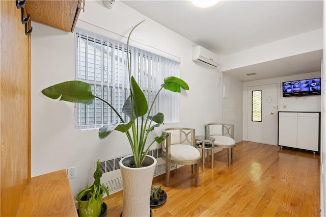 living area featuring light wood-type flooring, an AC wall unit, and radiator