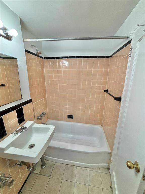 bathroom featuring sink, tiled shower / bath combo, tile patterned flooring, and tile walls