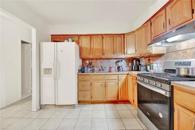 kitchen featuring tasteful backsplash, light tile patterned floors, white fridge with ice dispenser, gas range, and sink