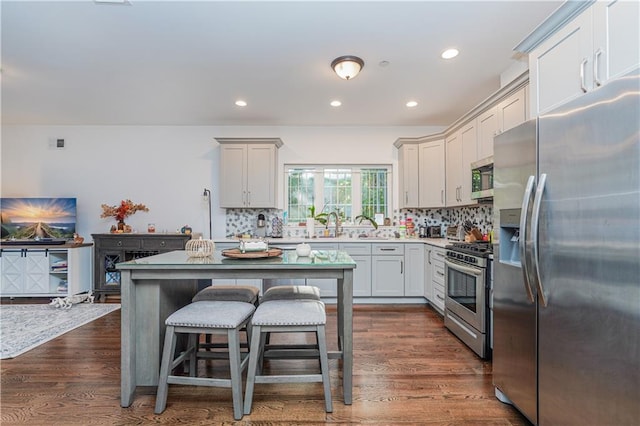 kitchen with appliances with stainless steel finishes, a breakfast bar area, dark hardwood / wood-style flooring, decorative backsplash, and a center island