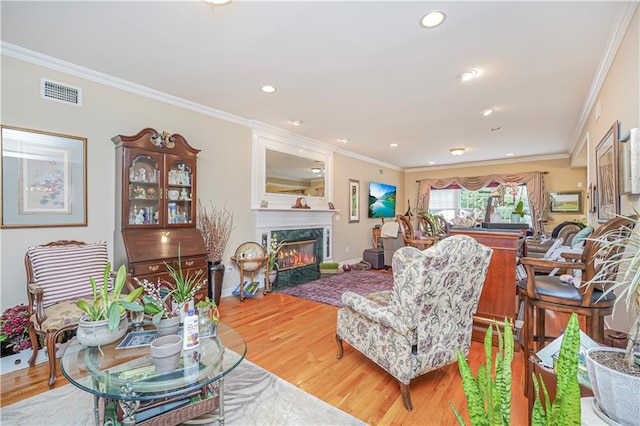 living area featuring a high end fireplace, crown molding, light wood finished floors, and visible vents