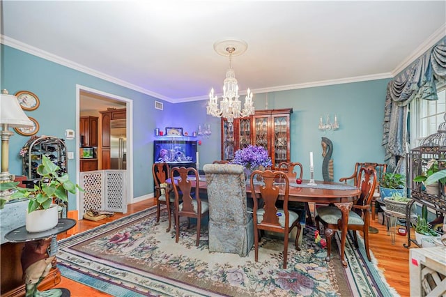 dining space with an inviting chandelier, crown molding, wood finished floors, and visible vents