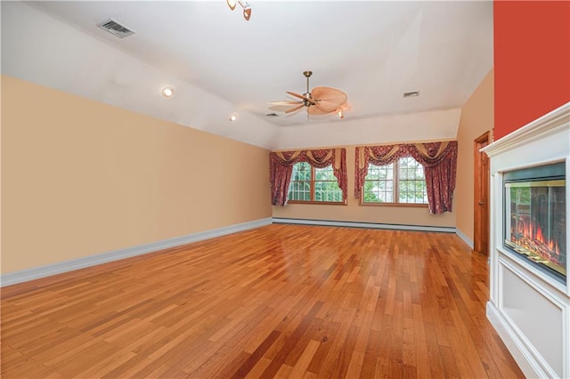 unfurnished living room with baseboard heating, vaulted ceiling, light wood-style flooring, and visible vents
