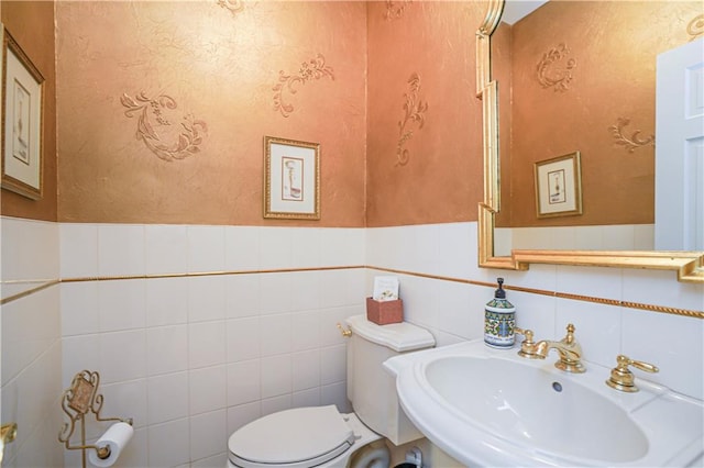 half bathroom with a sink, wainscoting, toilet, and tile walls