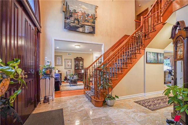 entryway featuring a high ceiling, baseboards, marble finish floor, ornamental molding, and stairs
