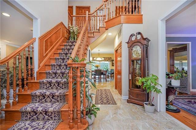 staircase with visible vents, crown molding, marble finish floor, a towering ceiling, and a notable chandelier