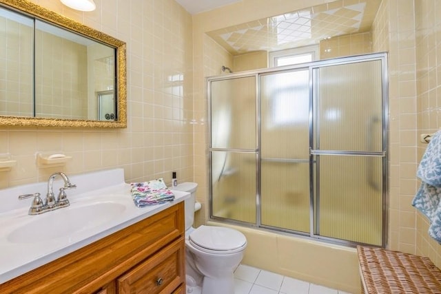 full bathroom featuring tile patterned floors, toilet, shower / bath combination with glass door, tile walls, and vanity