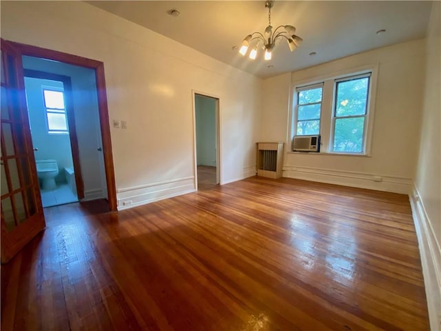 spare room featuring an inviting chandelier, hardwood / wood-style floors, radiator heating unit, and a wealth of natural light