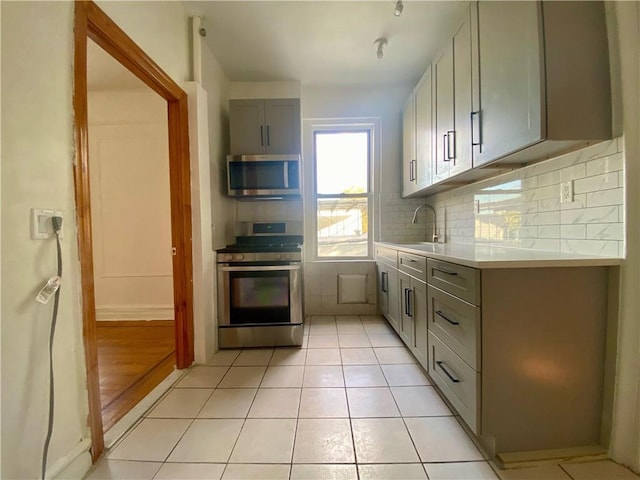 kitchen featuring decorative backsplash, appliances with stainless steel finishes, light hardwood / wood-style flooring, gray cabinetry, and sink